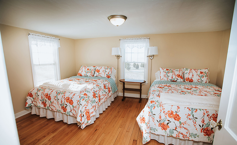 Picture of one of the bedrooms at Grandma's House at Circle K Farm, which contains two beds with flower patterened linens, two lamps, and a ceiling light